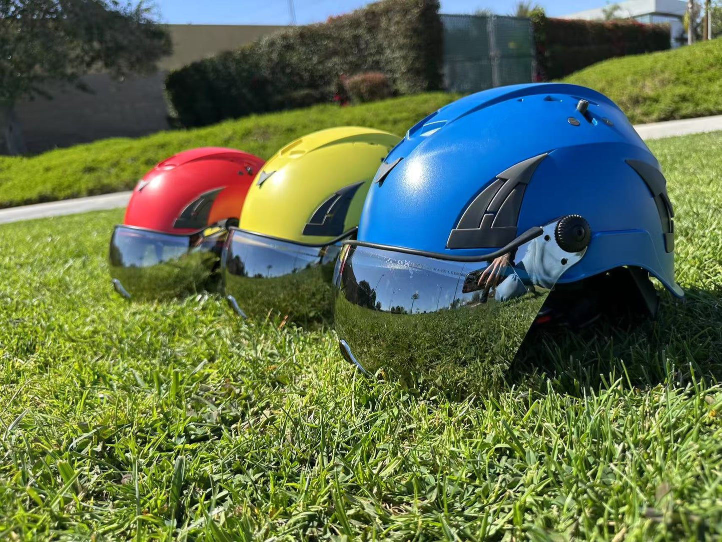 Low angle of three AeroPro Safety Helmets with Smoke Visor Kit, colors yellow, red and blue on Grass. Three ANSI/ISEA Z89.1-2014 Type 1 Class C Safety Helmets with Smoke Visor used for Industrial, Rescue & fall protection. 