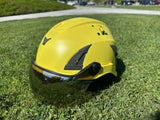 Front side view of AeroPro Yellow ANSI/ISEA Z89.1-2014 Type 1 Class C Safety Helmets with Smoke Visor used for Industrial, Rescue & fall protection sitting on grass. 