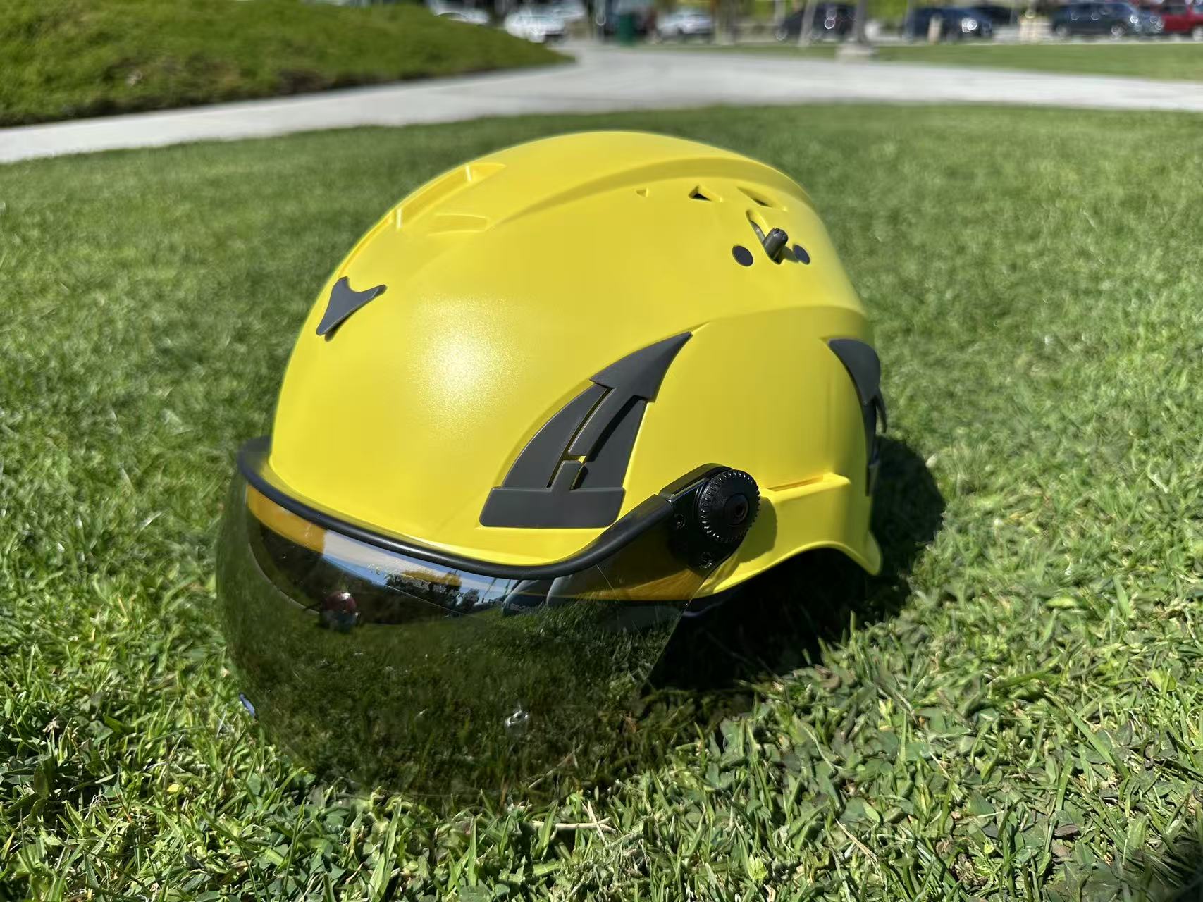 Front side view of AeroPro Yellow ANSI/ISEA Z89.1-2014 Type 1 Class C Safety Helmets with Smoke Visor used for Industrial, Rescue & fall protection sitting on grass. 