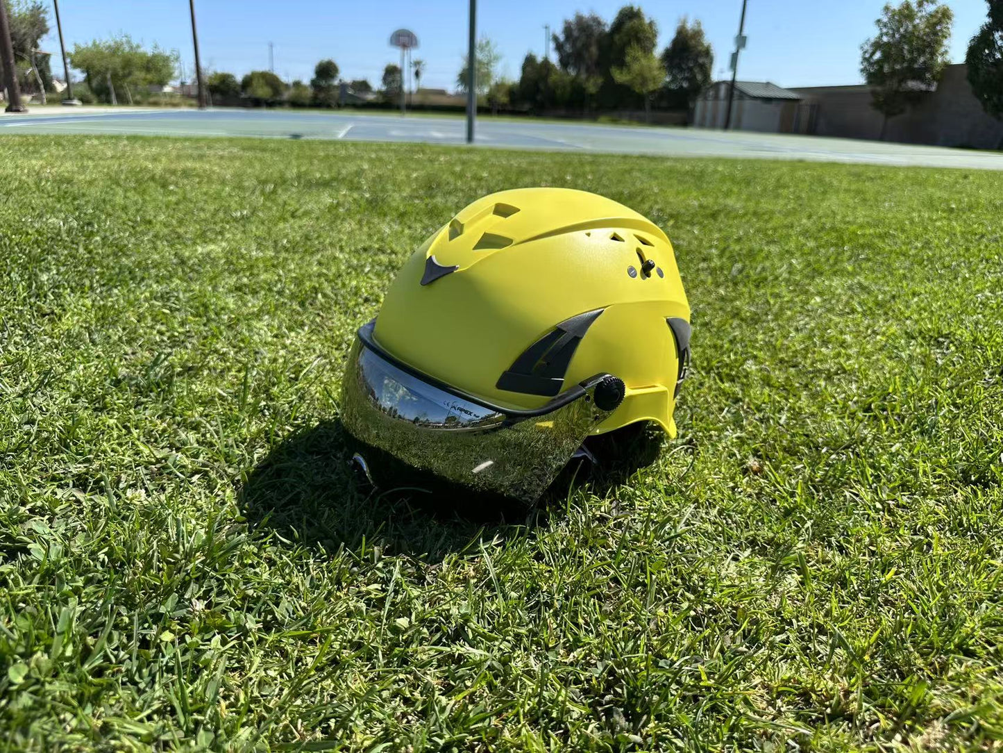 Low angle side view of AeroPro Yellow ANSI/ISEA Z89.1-2014 Type 1 Class C Safety Helmets with Smoke Visor used for Industrial, Rescue & fall protection sitting on grass. 
