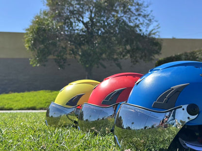 Low angle side view of three AeroPro Safety Helmets with Smoke Visor Kit, colors yellow, red and blue on Grass. Three ANSI/ISEA Z89.1-2014 Type 1 Class C Safety Helmets with Smoke Visor used for Construction, Rescue & Arborist. 